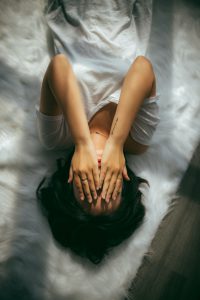 Mujer acostada boca arriba en la cama, tapándose la cara con las dos manos como nerviosa y ansiosa. Como tratar la ansiedad, como tratar la depresión, tratar el estrés, alimentación sana, relación del nervio vago con la ansiedad, como cuidar el nervio vago, técnicas de relajación.