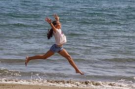 Mujer corriendo y dando un gran salto por la orilla de la playa como demostrando su felicidad y acentuando esa actitud positiva que le ayudará a combatir la ansiedad al dormir, estrés y la depresión.