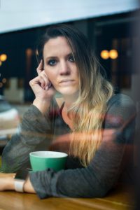 Foto de una mujer apoyada en una mesa tomando té con un semblante pensativo y ansiosa. Como tratar la ansiedad, como tratar la depresión, tratar el estrés, alimentación sana, relación del nervio vago con la ansiedad, como cuidar el nervio vago, técnicas de relajación.