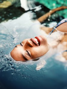 Foto de una mujer flotando sobre el agua que se le ve el rostro con una piel sana y bonita emergente del agua.