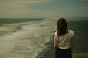 Foto de una mujer de espaldas mirando el romper de las olas y con un semblante de pensativa. Como tratar la ansiedad, como tratar la depresión, tratar el estrés, alimentación sana, relación del nervio vago con la ansiedad, como cuidar el nervio vago, técnicas de relajación.