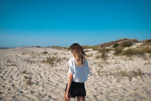 Mujer que se ve de espaldas andando por la arena hacía la playa. 