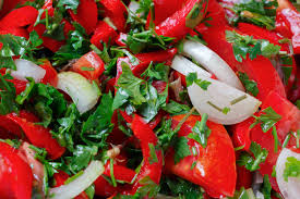 Plato de verdura que contiene pimiento rojo troceado con cebolla y perejil.